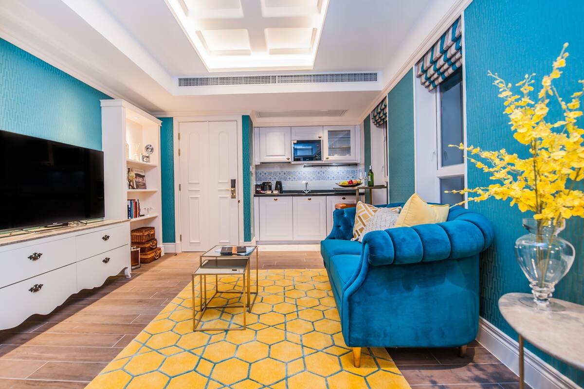 Una sala de estar moderna con un sofá azul, un televisor de pantalla plana y un tapete amarillo estampado.