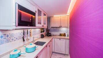 Una cocina con armarios blancos, microondas, fregadero y encimera con una olla azul y un hervidor.