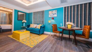 A modern living room with a blue sofa, yellow ottoman, and a dining area with a table and chairs.