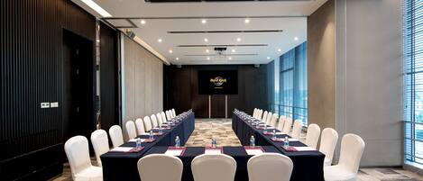 A conference room with a long table, white chairs, and a projector screen.
