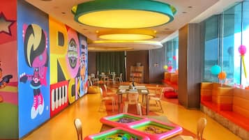 A brightly colored children's play area with inflatable pools, a large mural, and a seating area with orange cushions.