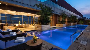 Un área de piscina moderna con sillas de descanso, una jardinera grande con follaje y una fachada de edificio contemporánea.