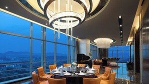 A high-rise hotel dining area with a round table set for six, large windows offering a city view, and a grand chandelier. - Hard Rock Hotel Shenzhen (Shenzhen)