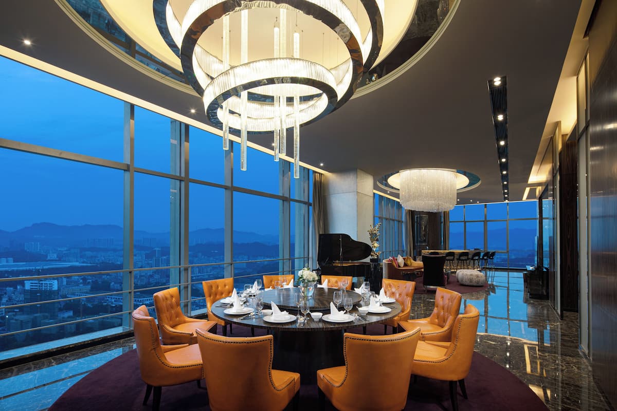 Comedor de un hotel de gran altura con una mesa redonda para seis personas, ventanas amplias que dan a vistas de la ciudad y una imponente lámpara de araña.