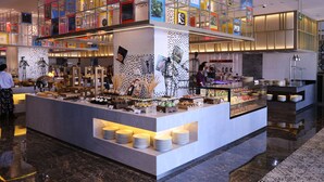 A modern hotel lobby with a central buffet area, a glass display wall, and a seating area with tables and chairs. - Hard Rock Hotel Shenzhen (Shenzhen)