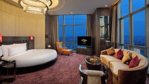A hotel room with a large bed, a sofa, a TV, and a city view. - Hard Rock Hotel Shenzhen (Shenzhen)