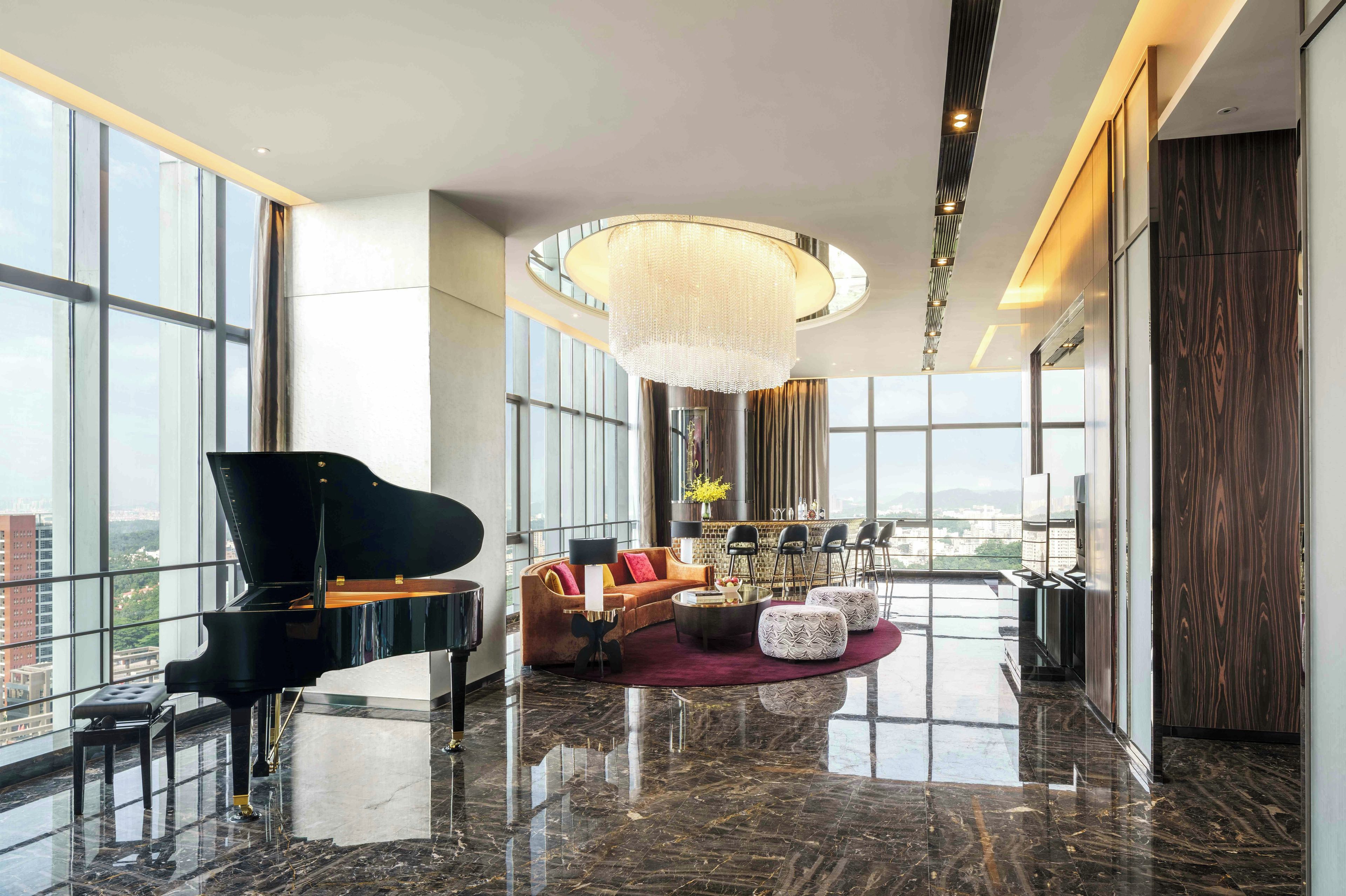 A spacious living area with a grand piano, a modern chandelier, and a city view.