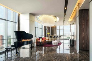 Amplia sala de estar con un piano de cola, una lámpara moderna y vistas a la ciudad.
