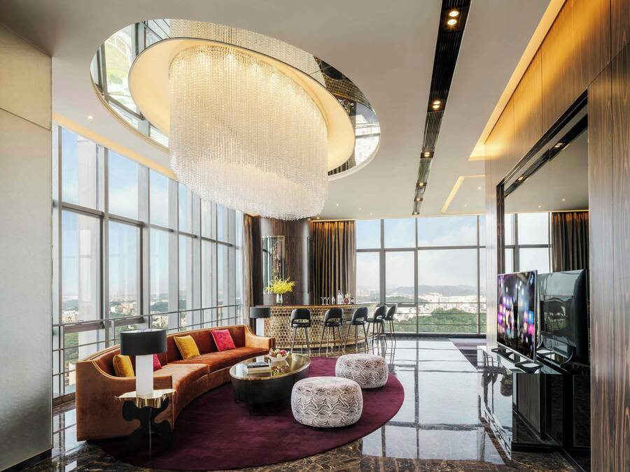 A spacious living room with a large chandelier, a sofa set, a bar area, and a television.