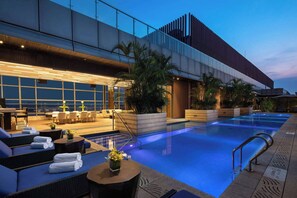 Un hotel moderno con zona de piscina, mobiliario exterior y una entrada bien iluminada.