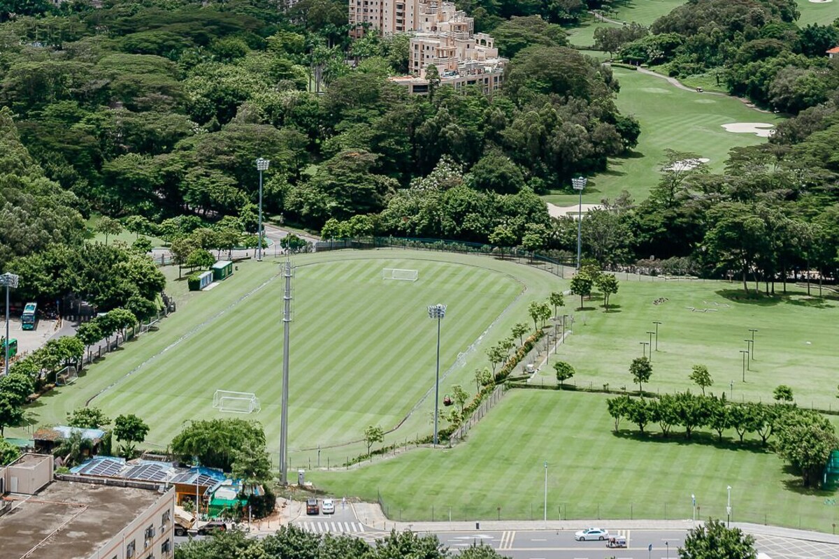 Campo de golf con un edificio grande en el centro, rodeado de vegetación y un paisaje urbano al fondo.