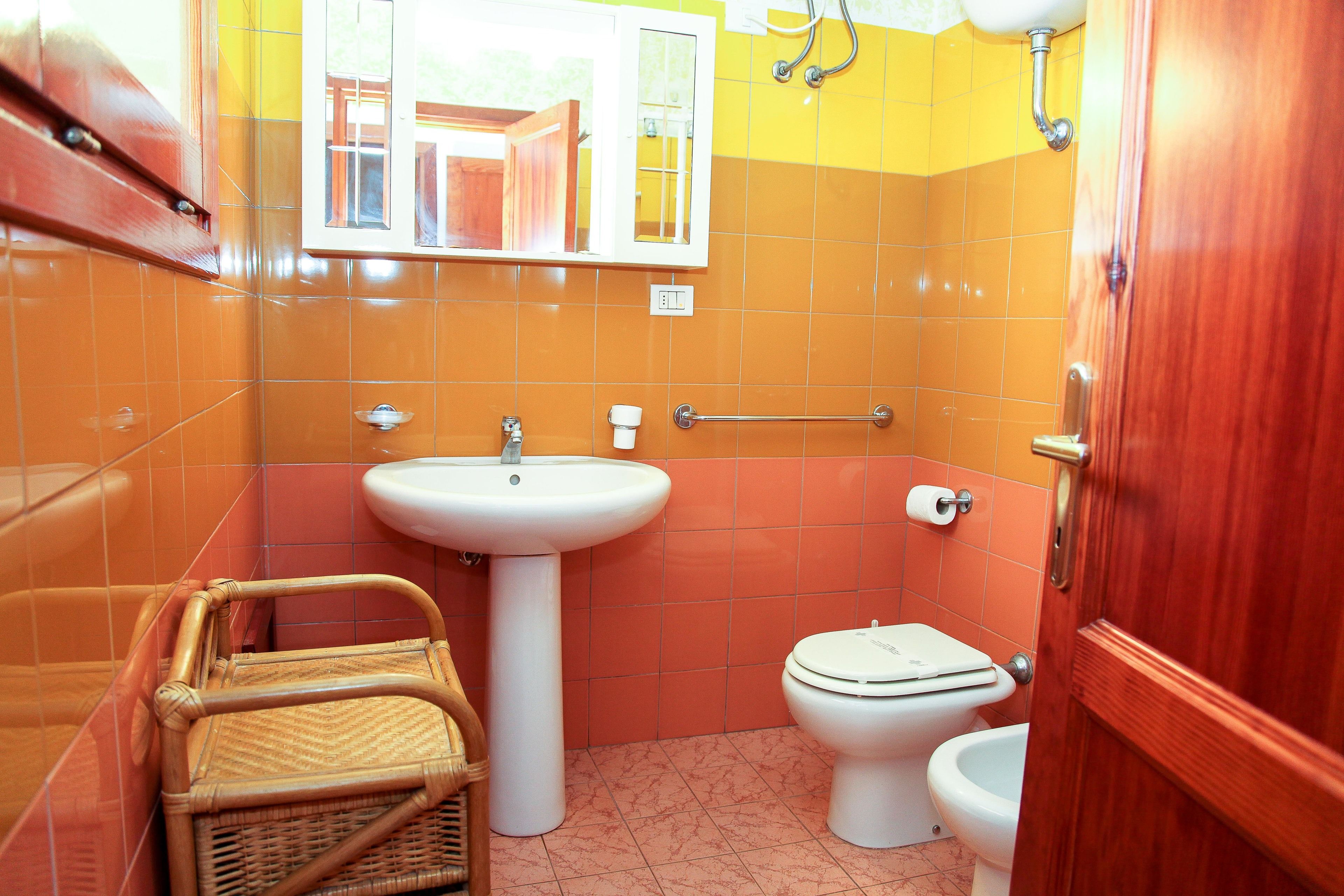 Een badkamer met een wastafel, toilet en bidet, een raam en een houten deur.