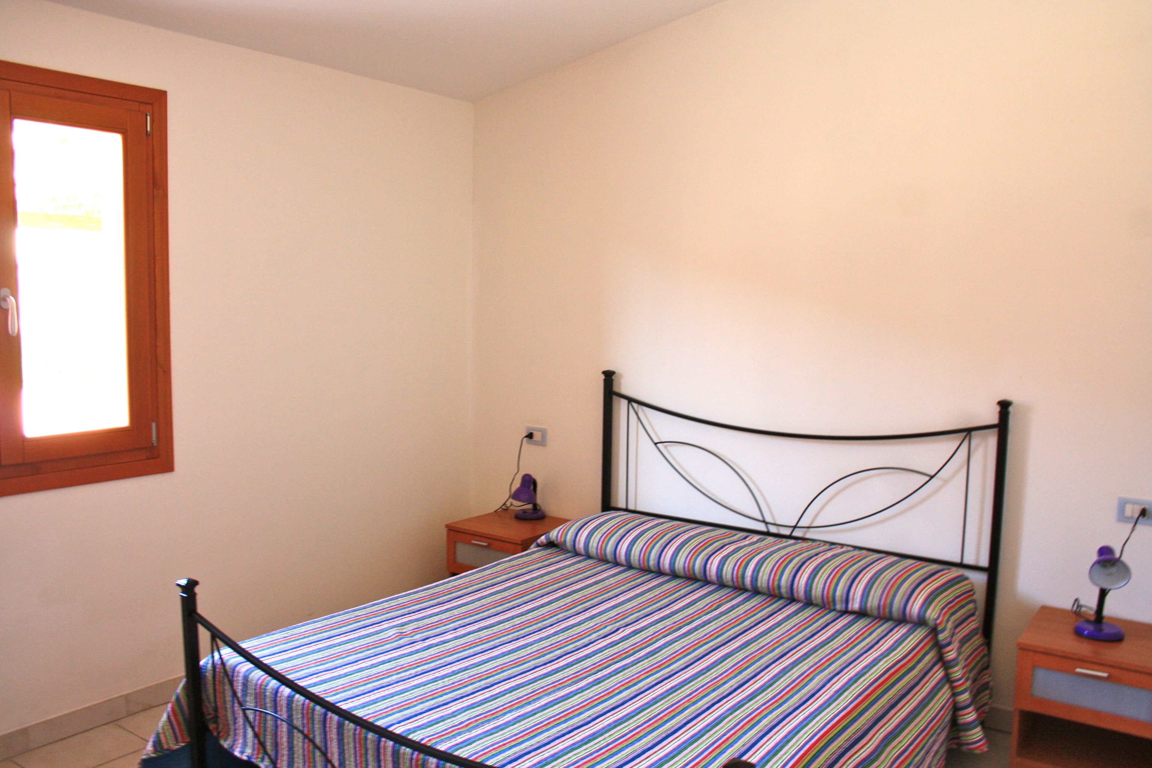 A bedroom with a bed, a nightstand, a lamp, and a window.