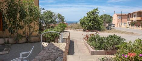 A residential street with houses, a paved sidewalk, and a view of the sea.