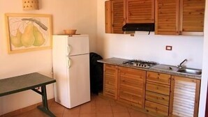 A compact kitchen with wooden cabinets, a white refrigerator, a stove, and a sink.