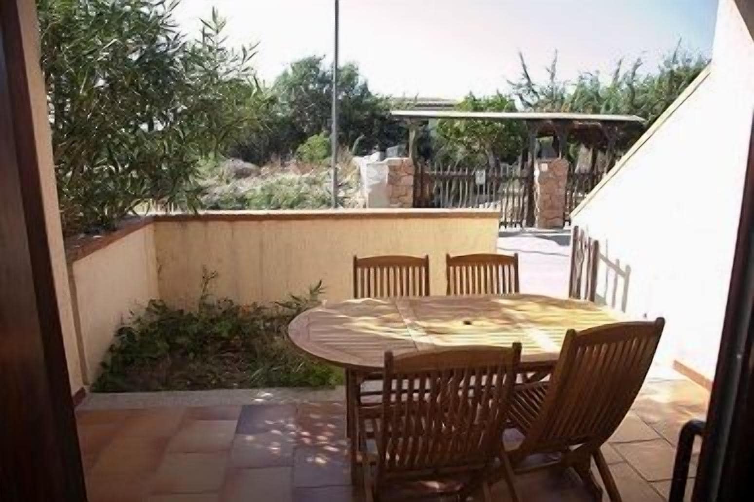 A patio with a round table and chairs, surrounded by a low stone wall and vegetation.