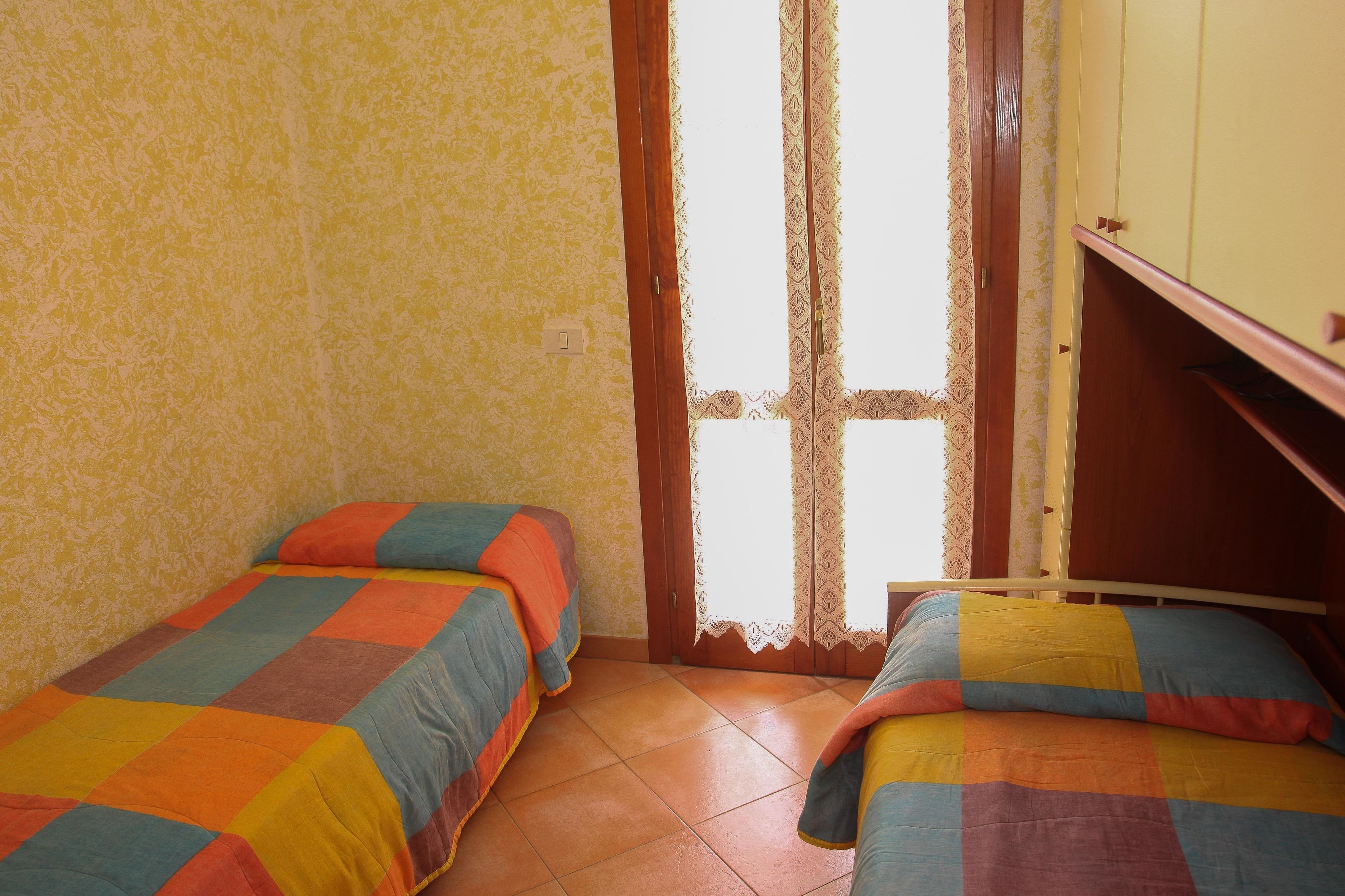 Un dormitorio con dos camas individuales, un armario de madera y una cortina de encaje.