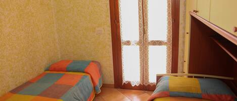 Un dormitorio con dos camas individuales, un armario de madera y una cortina de encaje.