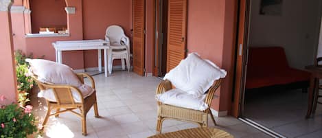 A room with wicker furniture, a white table, and a red chair.