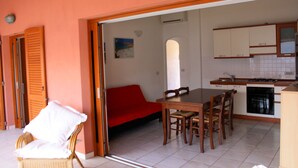 A compact kitchen with a dining area, a red sofa, and a wicker chair.
