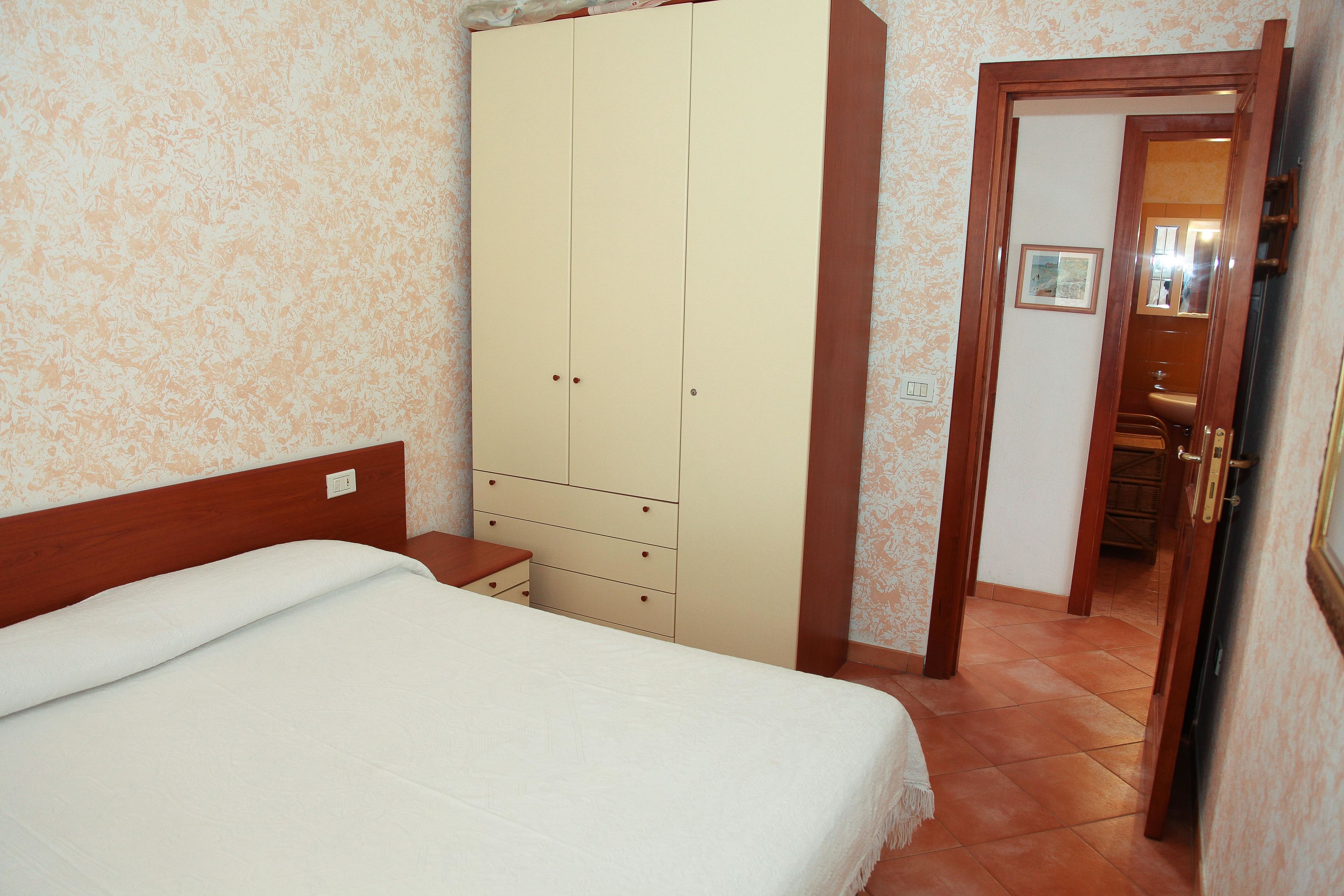 Een slaapkamer met een bed, een kledingkast en een badkamer, zichtbaar door een geopende deur.