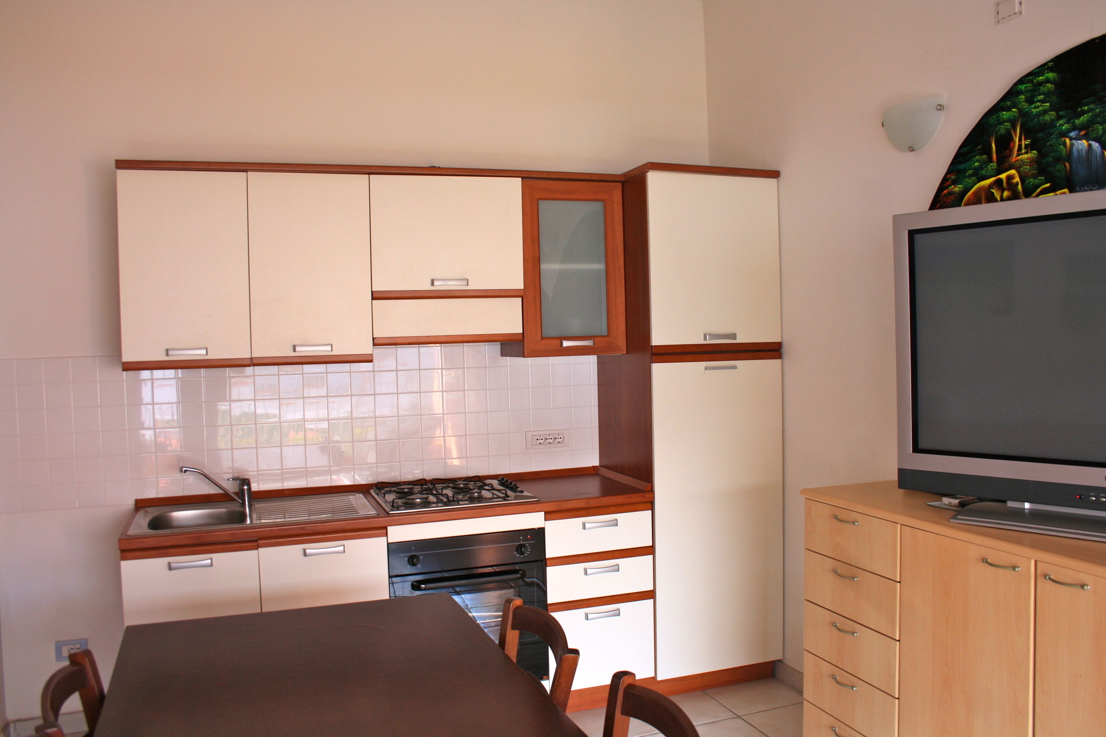 A compact kitchen with white cabinets, a stove, oven, and a TV on a wooden cabinet.