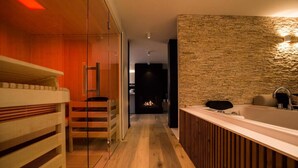 A modern bathroom with a wooden floor, a glass shower enclosure, a wooden bench, a large bathtub, and a stone-textured wall. - Wellness Hasselt Bed & Breakfast (Hasselt)