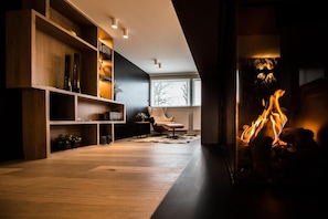 A modern living room with a fireplace, wooden shelving, and a comfortable chair. - Wellness Hasselt Bed & Breakfast (Hasselt)