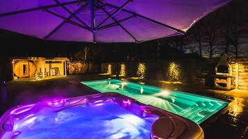 A hot tub and a pool area with a canopy and illuminated structures in the background.