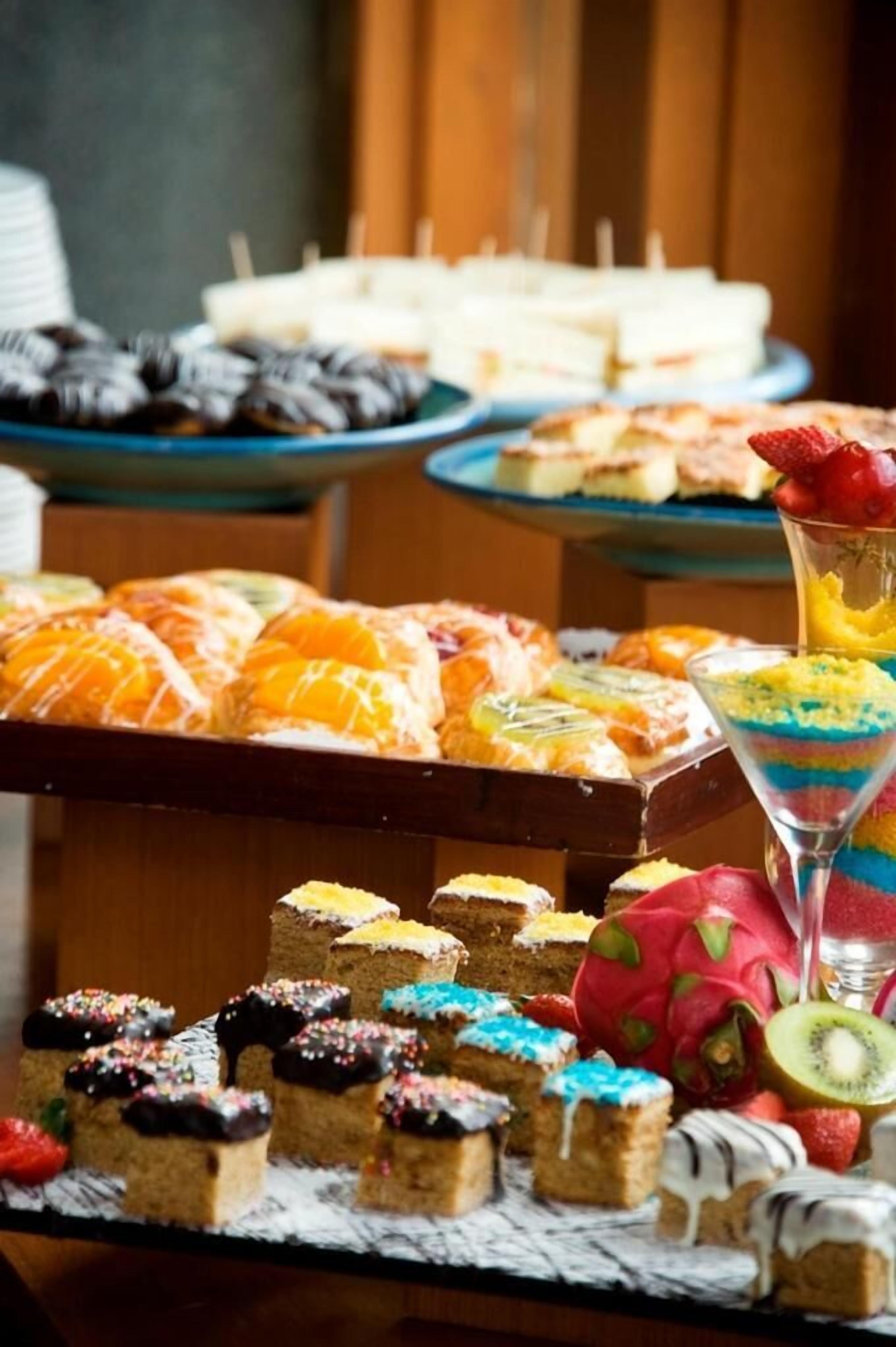 Variedad de postres en una mesa de buffet, incluyendo pasteles, productos de pastelería y un postre en capas en vaso.