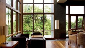 A spacious room with large windows offering a view of lush greenery. There are several seating areas with tables and chairs. - SanGria Resort & Spa (Lembang)