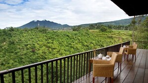 A wooden deck with wicker furniture overlooking a lush green landscape and a mountain in the distance. - SanGria Resort & Spa (Lembang)