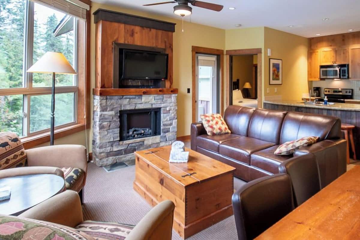 A cozy living room with a stone fireplace, leather sofa, and a wooden coffee table.