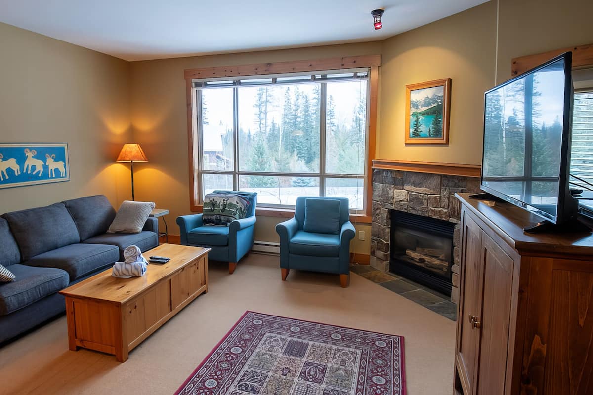 A cozy living room with a sofa, two armchairs, a coffee table, a fireplace, and a television.