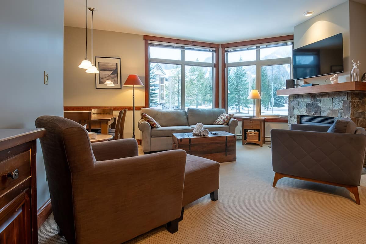 A spacious living room with a fireplace, large windows, and a cozy seating area.