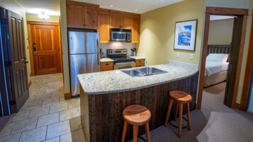 Una cocina con armarios de madera, electrodomésticos de acero inoxidable, encimera de granito y dos taburetes.