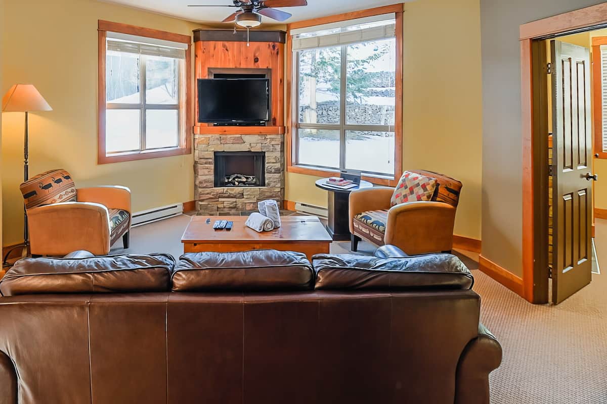 A cozy living room with a stone fireplace, leather sofa, and two armchairs.