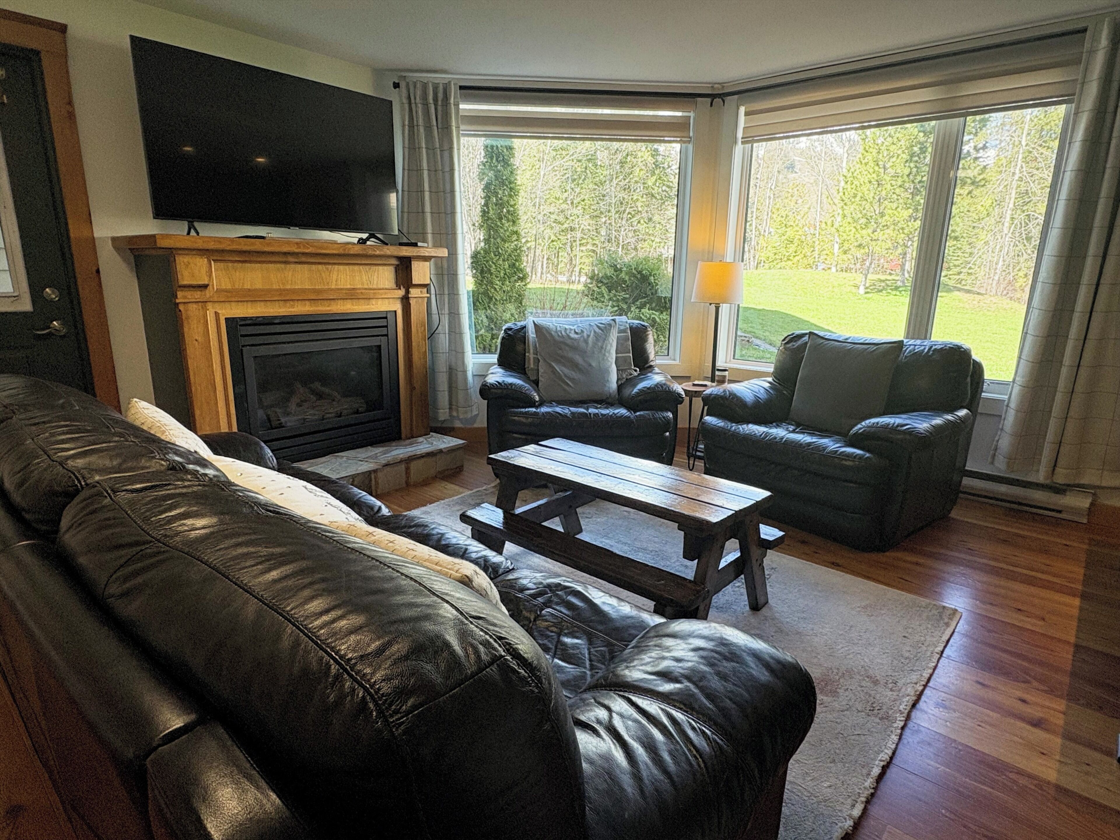 A living room with a fireplace, leather sofa, and two armchairs.