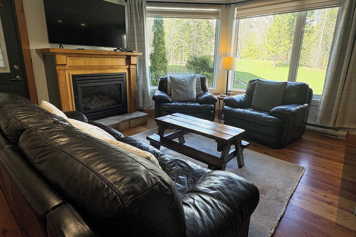 A living room with a fireplace, leather sofa, and two armchairs.