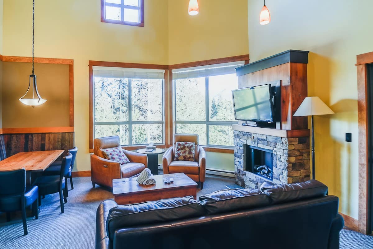 A cozy living room with a stone fireplace, comfortable seating, and large windows.