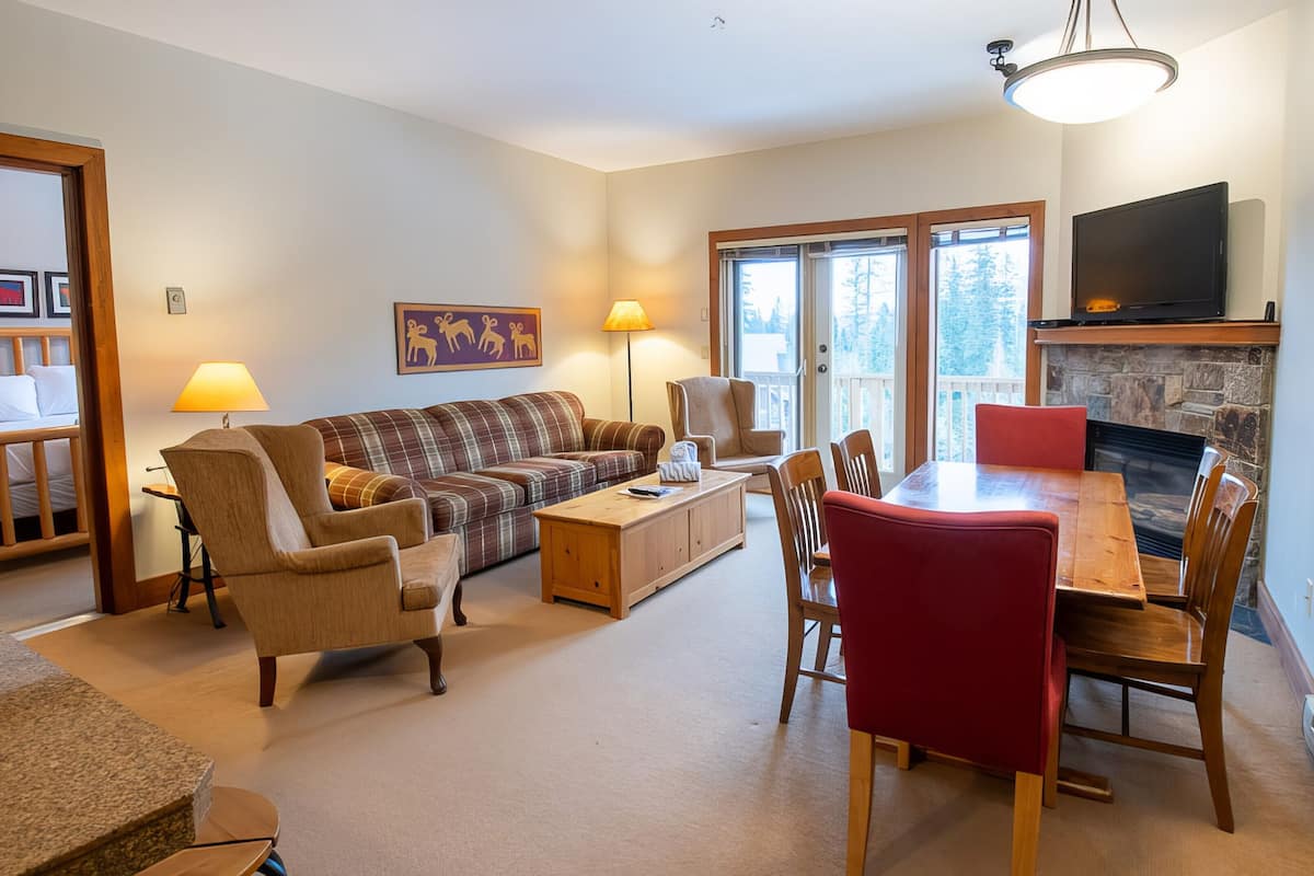A cozy living room with a sofa, armchairs, a dining table, and a fireplace.