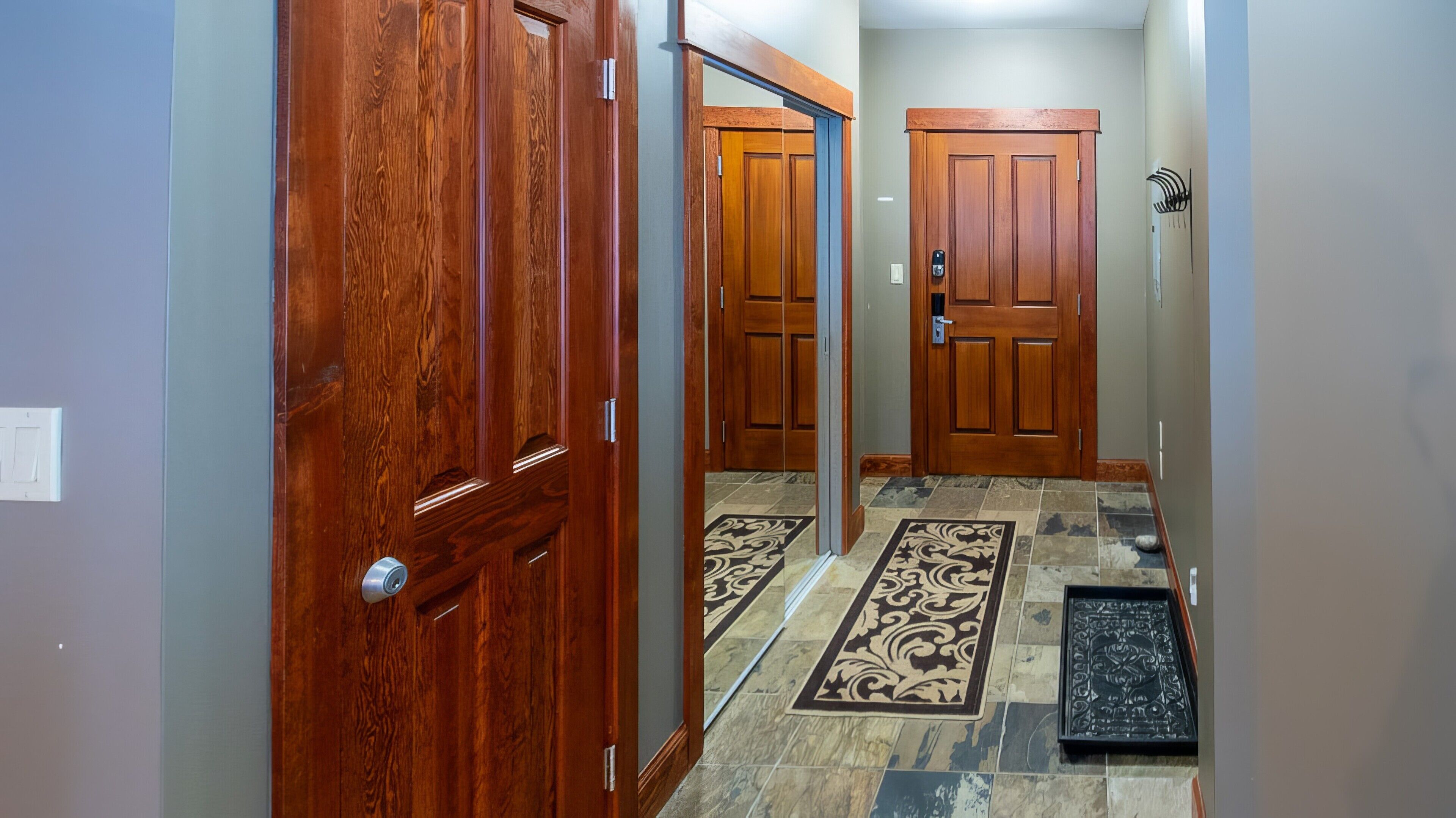 A hallway with wooden doors, a patterned rug, and a metal doormat.