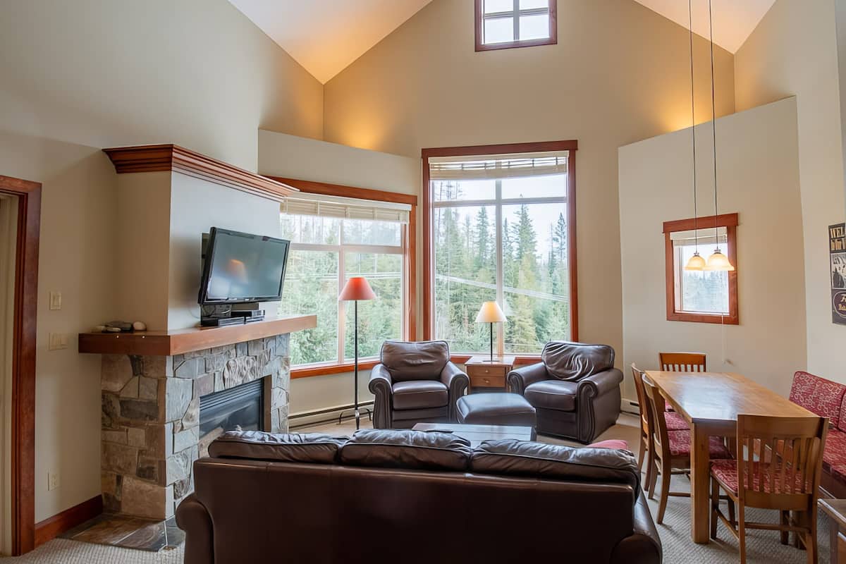 A cozy living room with a stone fireplace, leather sofa, and a television on a wooden shelf.