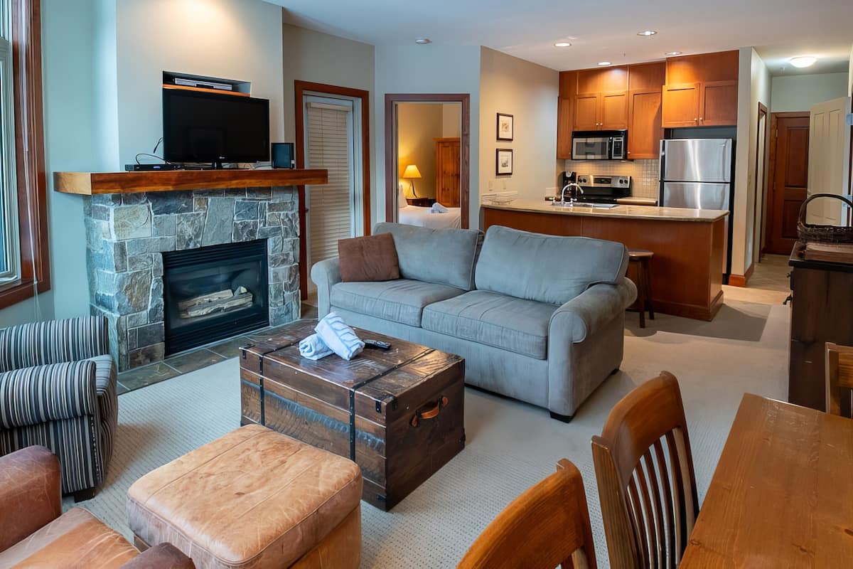 A modern living room with a stone fireplace, a grey sofa, a striped couch, and a wooden coffee table.