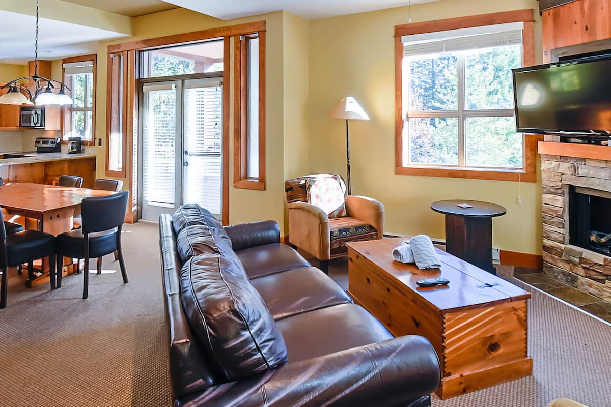 A spacious living area with a leather sofa, a wooden coffee table, a dining table with chairs, a fireplace, and a television.