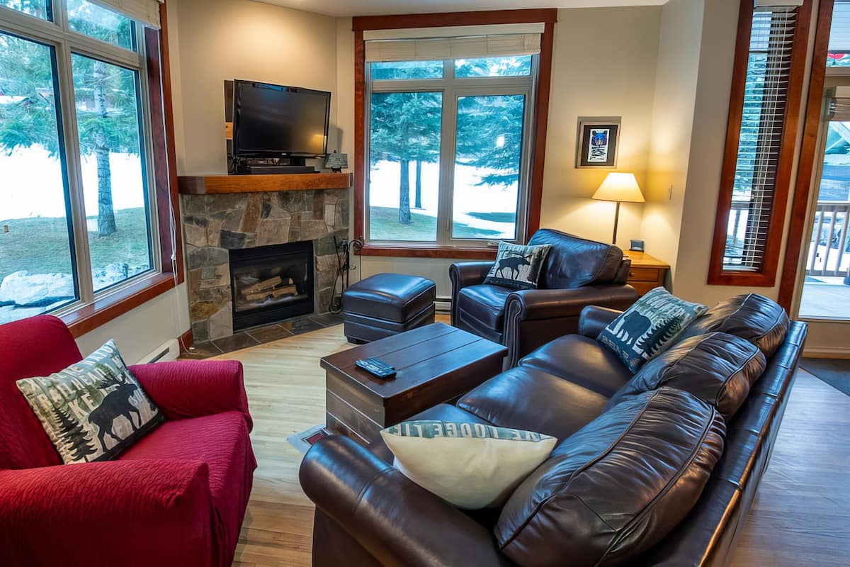 A living room with a stone fireplace, leather sofa, and red armchair.