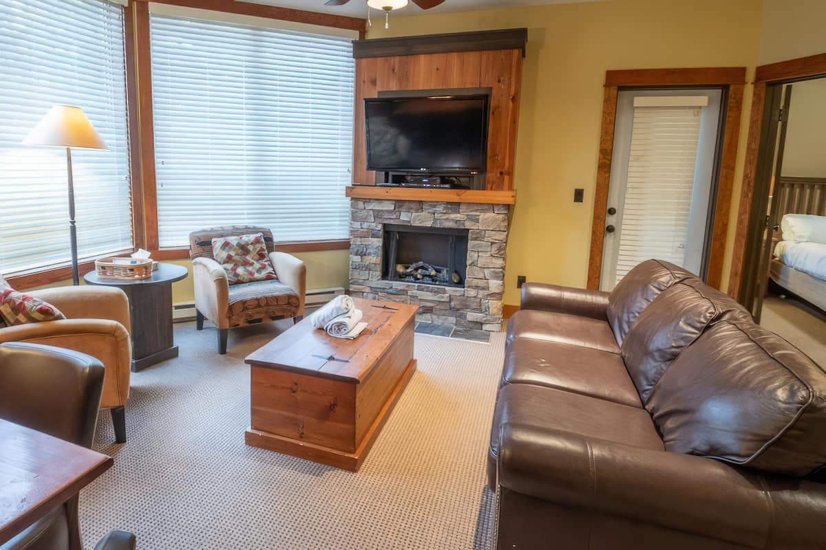 A living room with a stone fireplace, leather sofa, and a television mounted above it.