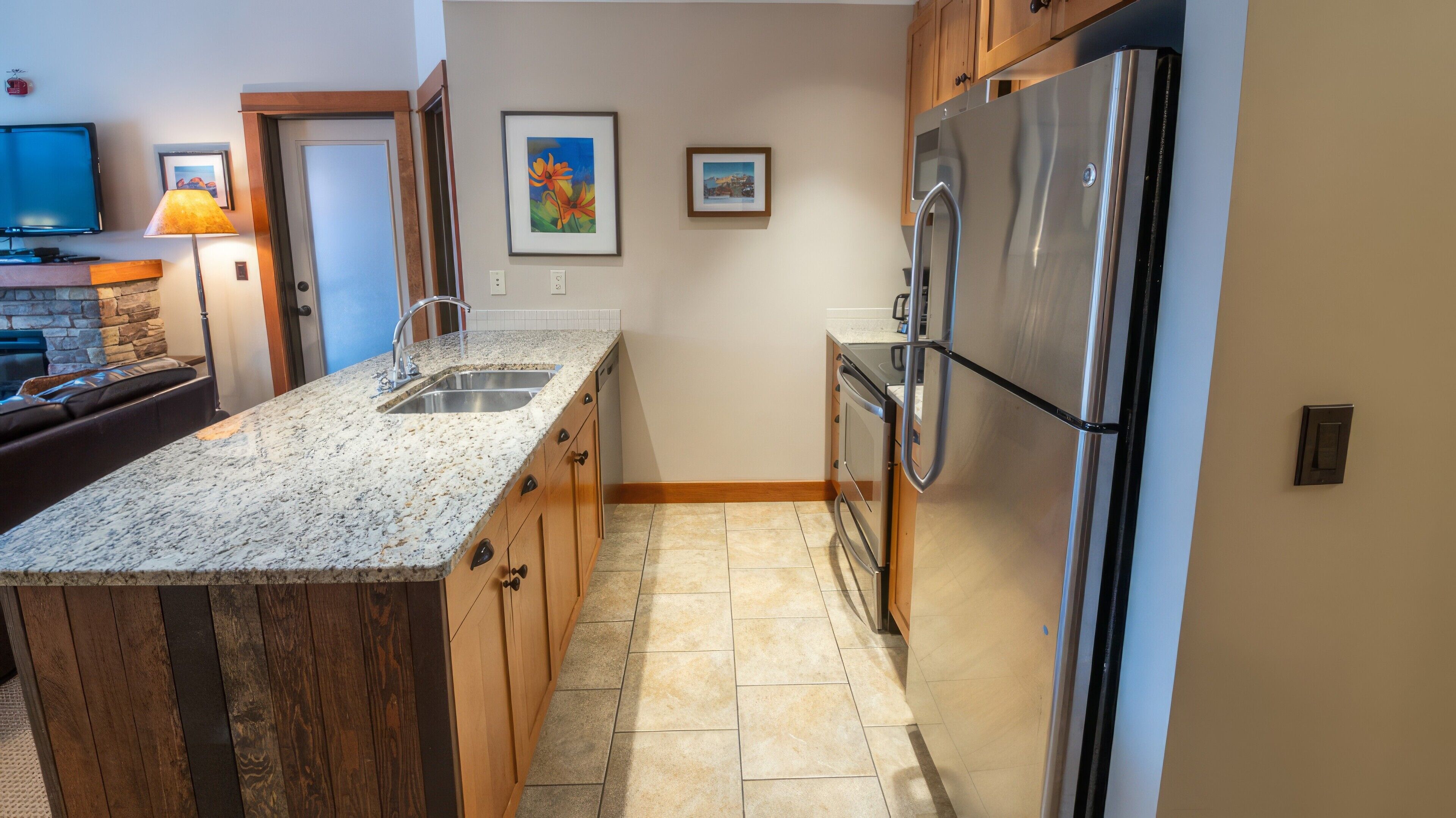 Una cocina con encimeras de granito, armarios de madera, un refrigerador de acero inoxidable y un horno empotrado.