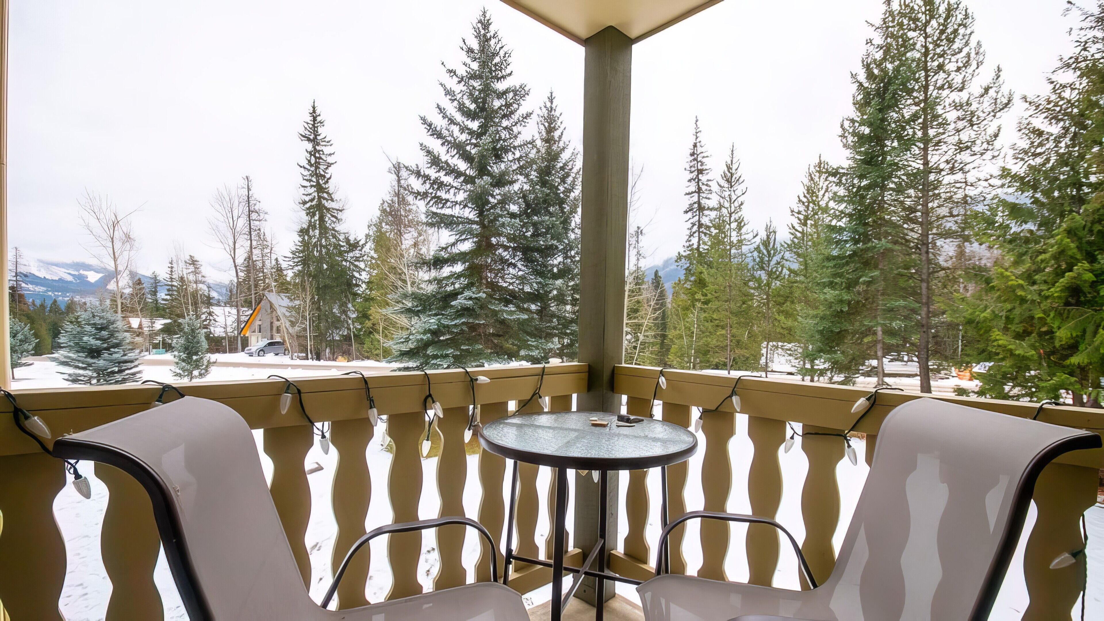 Ein Balkon mit Tisch und Stühlen, der auf eine verschneite Landschaft mit Bäumen und Bergen blickt.