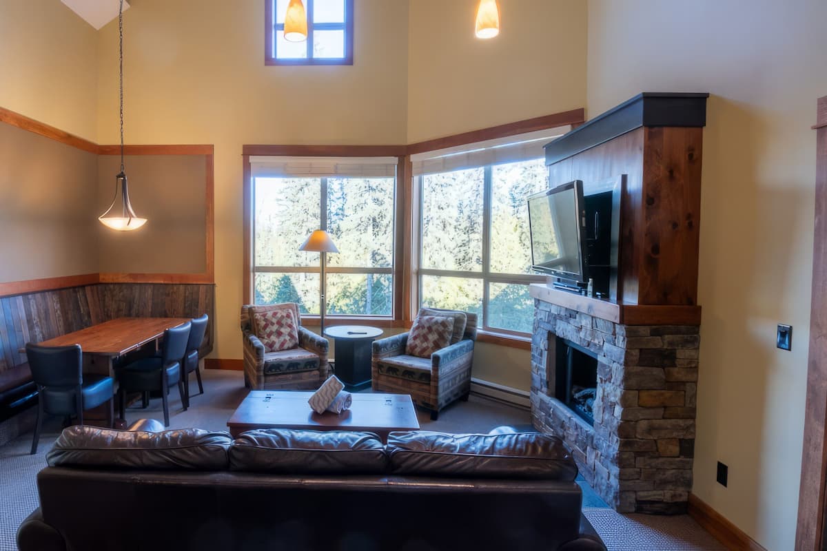 A cozy living room with a stone fireplace, a large TV mounted on the wall, and a comfortable seating area with a sofa and chairs.